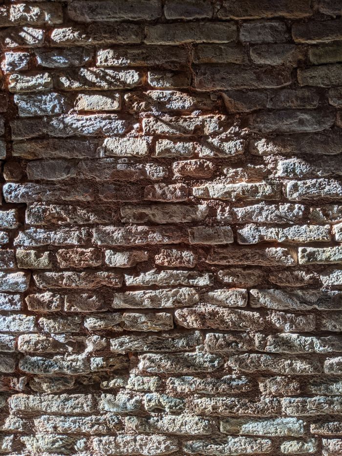 Close-up of a Venetian brick wall with sunlight casting shadows, showcasing texture and architectural style.
