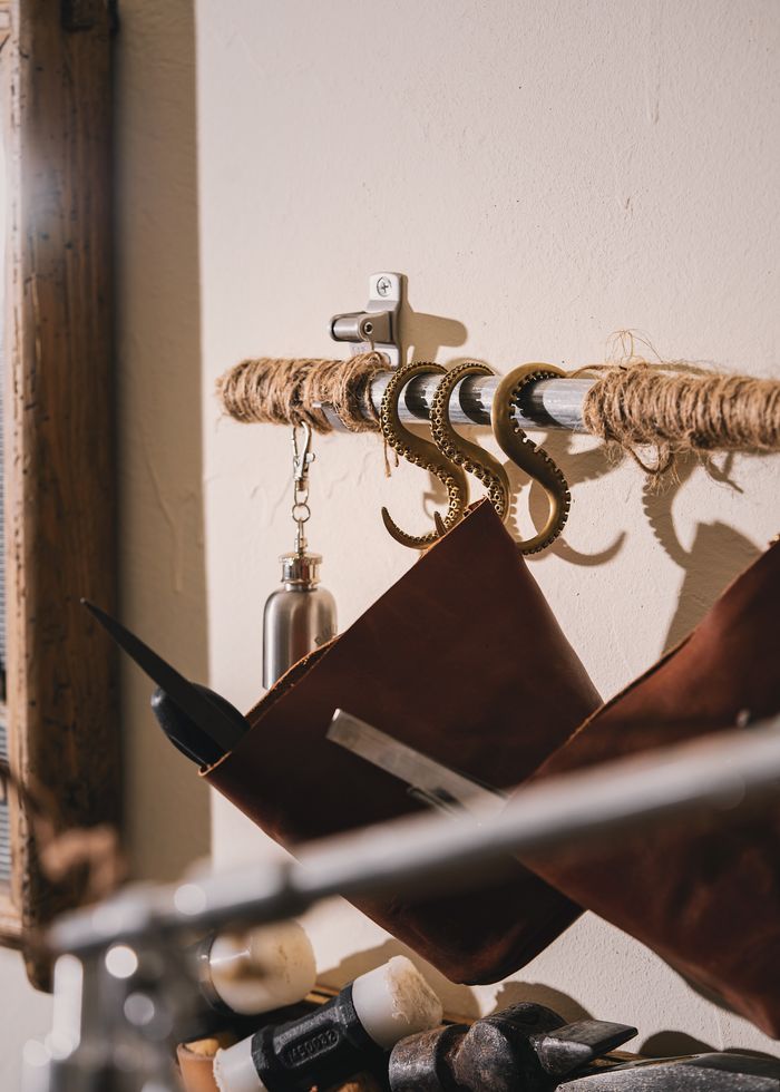 Close-up of a rustic hook rack in a workshop, featuring leather tools and vintage decor.