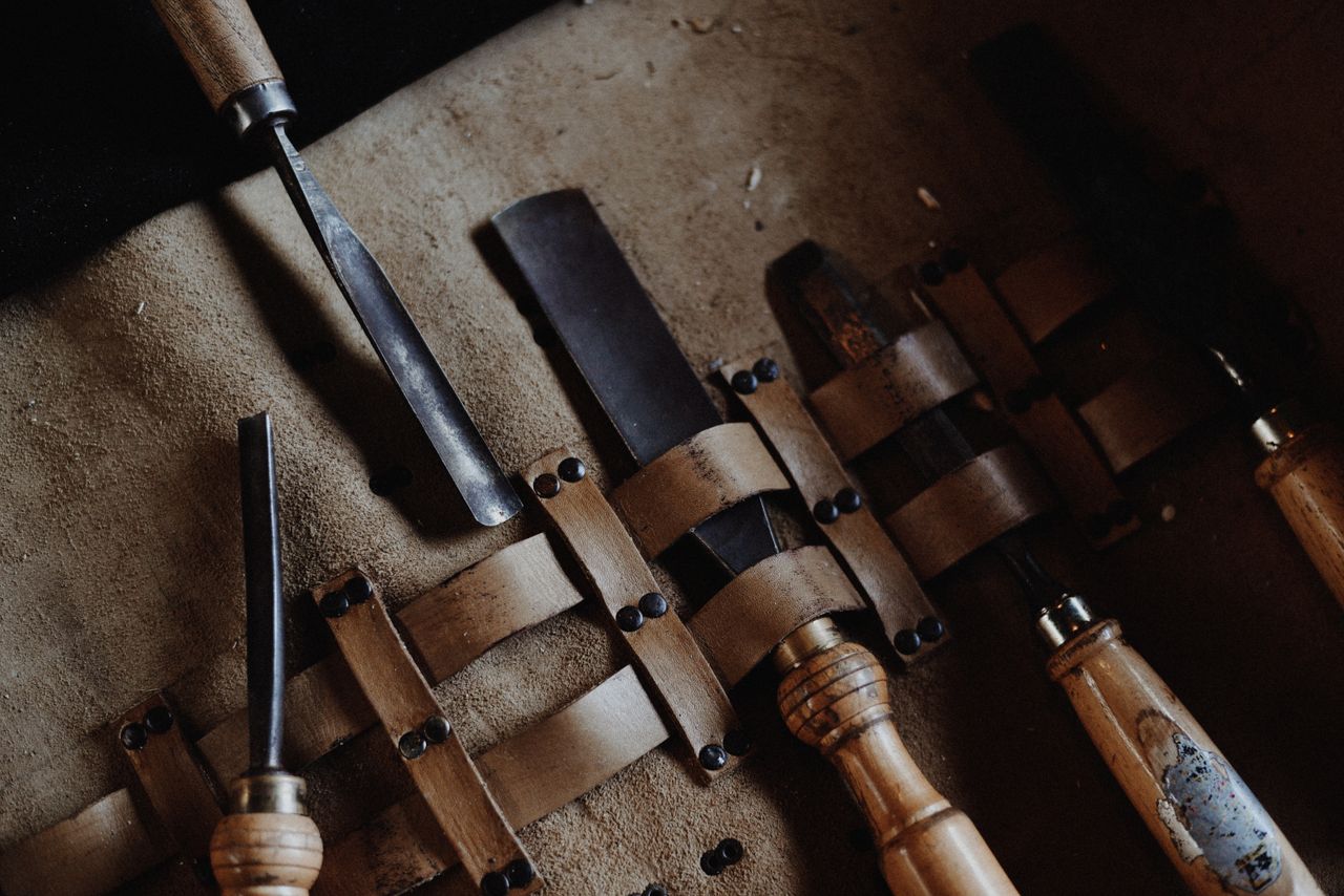 our-services-06 Set of vintage woodworking chisels neatly arranged on a rustic leather mat, showcasing craftsmanship.