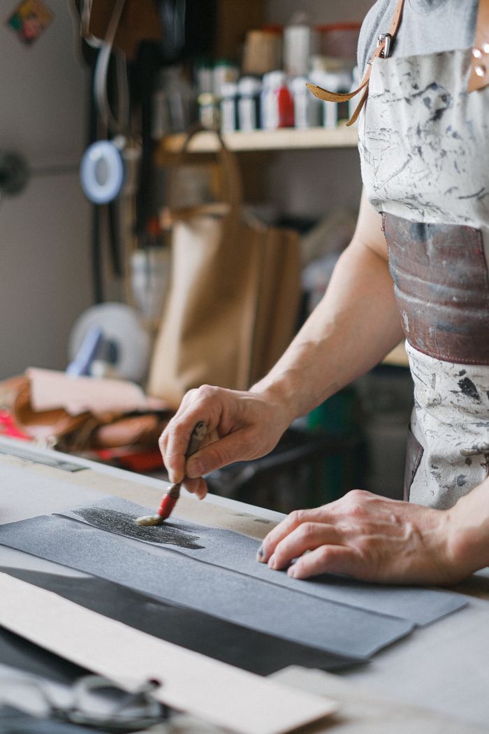 our-services-03 Focused artisan brushing leather in a workshop, highlighting craftsmanship and tactile artistry.