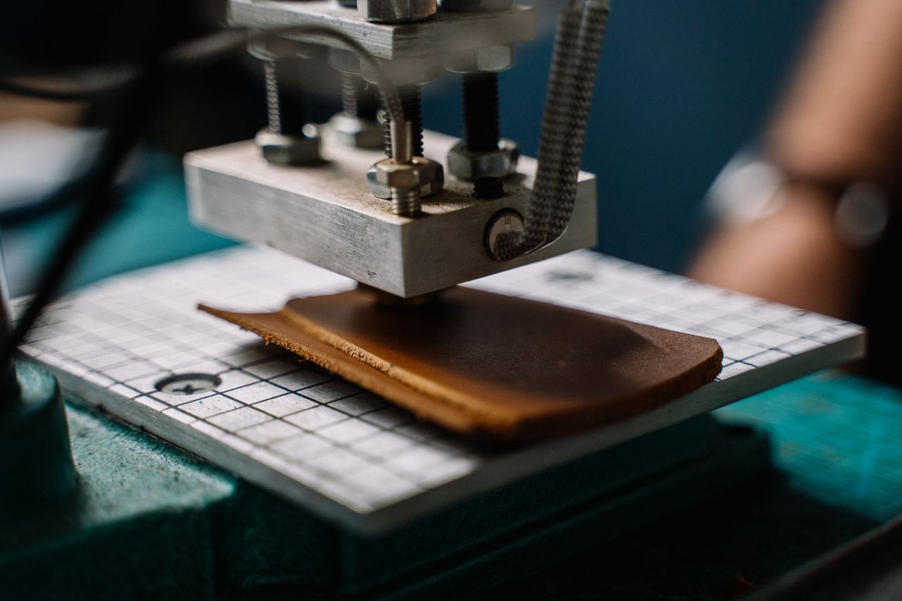 A close-up image showing a machine cutting leather in a workshop setting.