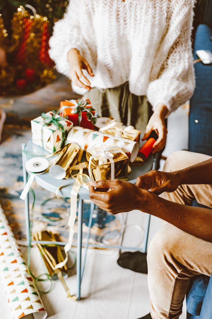 Two people wrapping Christmas gifts at home, creating a cozy holiday atmosphere.