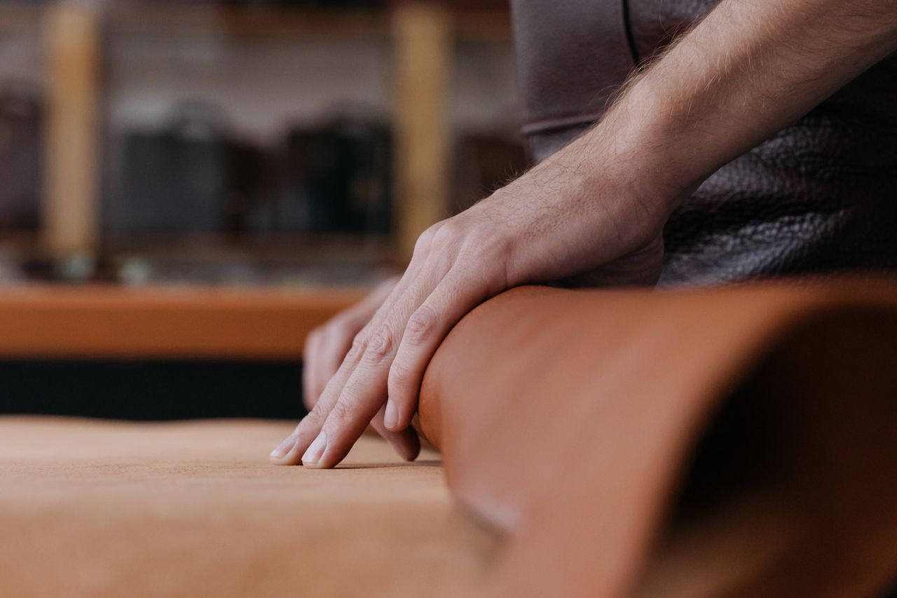 our-services-01 Close-up of hands working with leather in a workshop, emphasizing craftsmanship and detail.
